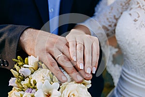 Close-up. Hand of bride and groom. Bride and groom hold hands. Focus on the rings. Bouquet in hand