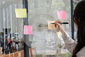 Close up hand businesswoman writing sticky notes on glass wall in office