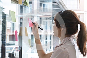 Close up hand businesswoman writing sticky notes on glass wall in office