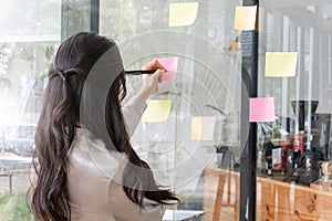 Close up hand businesswoman writing sticky notes on glass wall in office