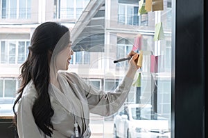 Close up hand businesswoman writing sticky notes on glass wall in office