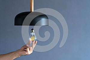Close-up. A hand changes a light bulb in a stylish loft lamp. Spiral filament lamp. Modern interior decor