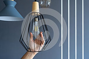 Close-up. A hand changes a light bulb in a stylish loft lamp. Spiral filament lamp. Modern interior decor