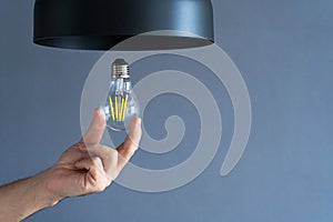 Close-up. A hand changes a light bulb in a stylish loft lamp. Spiral filament lamp. Modern interior decor