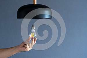 Close-up. A hand changes a light bulb in a stylish loft lamp. Spiral filament lamp. Modern interior decor