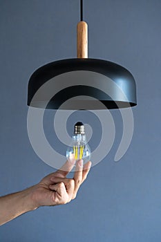 Close-up. A hand changes a light bulb in a stylish loft lamp. Spiral filament lamp. Modern interior decor