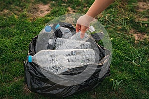 Close up hand collects plastic bottle in a park. A volunteer cleaning garbage.