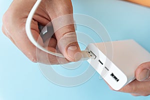 Close-up of a hand connecting a USB cable to a white power bank on a blue background.