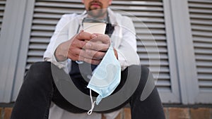 Close-up of hand with cup of coffee and protective medical mask. Tired, exhausted doctor in medical white coat during