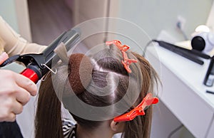 Close-up of a hand curling a strand of hair on a woman& x27;s head with tongs.