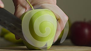 Close-up of hand cutting green apple with kitchen knife indoors