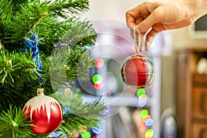 Close up hand decorating the chrismas tree with beautiful red ball toy f