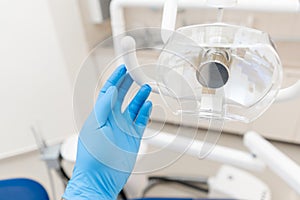 Close-up hand of dentist in the glove adjusts the lamp. . Office where dentist conducts inspection and concludes.