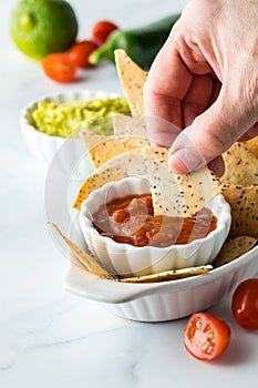 Close up of a hand dipping a keto diet baked tortilla chip into a bowl of salsa.
