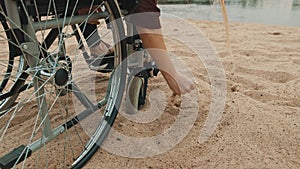 Close up, hand of disabled person in the wheelchair playing with the sand on the river coast. Vacation and travel with