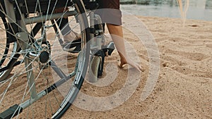 Close up, hand of disabled person in the wheelchair playing with the sand on the river coast. Vacation and travel with