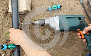 Close-up - hand drills a hole in the pipe. Installing drip irrigation in a farm with your own hands. Assembly of the drip irrigati