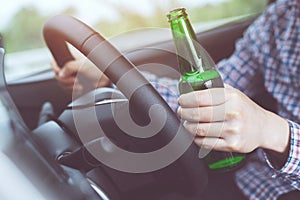 Close up hand Drunk young man while driving a car with a bottle of beer. Don`t drink and drive concept. Driving