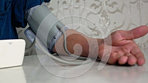 Close-up of the hand of an elderly man measuring blood pressure with a household tonometer while sitting at the table at home. A p