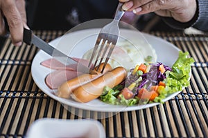 Close up hand on english breakfast - fried eggs, sausages, Ham a