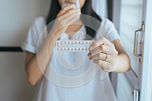 Close up of hand female holding birth control pill and a glass of water