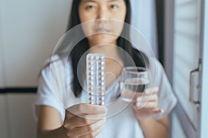 Close up of hand female holding birth control pill and a glass of water