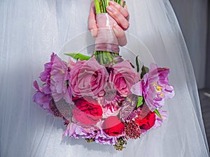 Close-up of the hand of girl in wedding dress who hold the bouquet of the bride.