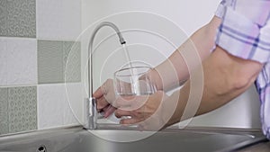 Close-up of hand with glass taking tap purified filtered water from special kitchen mixer