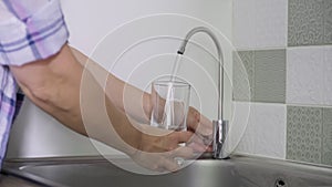 Close-up of hand with glass taking tap purified filtered water from special kitchen mixer