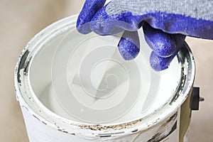 Close up of hand gloved painter mixing white paint with wooden stick