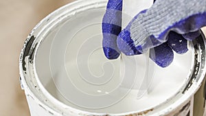 Close up of hand gloved painter mixing white paint with wooden stick