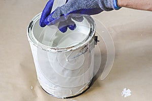 Close up of hand gloved painter mixing white paint with wooden stick