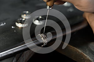 Close-up of hand of a goldsmith setting the diamond on the ring. Craft jewelery making with professional tools.