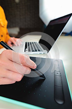 Close-up of a hand with a graphics tablet and a laptop, remote work at home. Graphic designer or architect at work desk