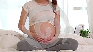 Close up hand Happy Pregnant Woman sitting on bed holding and stroking her big belly at home,Pregnancy of young woman enjoying