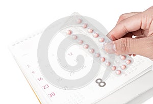 Close up hand hold birth-control pill with date of calendar back