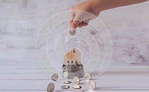 Close-up hand hold coin put in glass piggy bank jar with wooden house inside.Finance and property investment with bank loan and