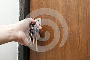 Close-up of a hand holding a bundle of different keys in key hole in wooden texture door.