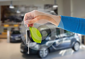 Close up of hand holding car key with green leaf