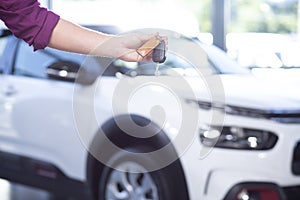 Close-up of a hand holding car keys with a blurred car in the ba