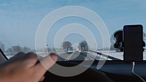 Close-up hand holding car steering wheel moving on winter road with mounted smartphone navigation app slow motion.