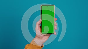Close up of Hand holding cell phone with green screen on blue studio background. Chroma key mockup on smartphone in hand