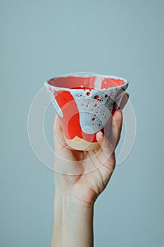 Close-up hand holding ceramic designer cup on grey background