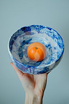 Close-up hand holding ceramic pottery bowl on grey background