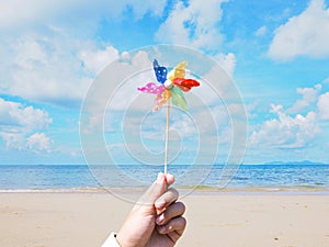Close up hand holding colorful pinwheel over summer beach background