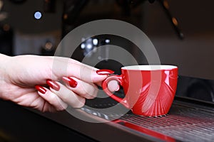 Close-up, hand holding a cup of coffee mugs is standing on the grill in the coffee maker, the background is blurred