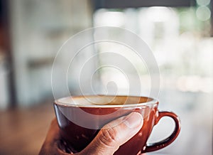 Close up hand holding a cup of hot cappuccino coffee cup with heart shape latte art blur cafe interior.food and drink concept.copy