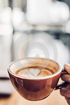 Close up hand holding a cup of hot cappuccino coffee cup with heart shape latte art blur cafe interior.food and drink concept.copy