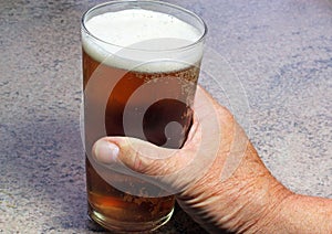 Close up of a hand holding drink in a pint glass.