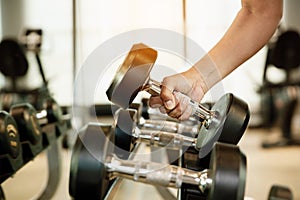 Close up hand holding dumbbell on floor in gym with woman background. Object goal weightlifting bodybuilding